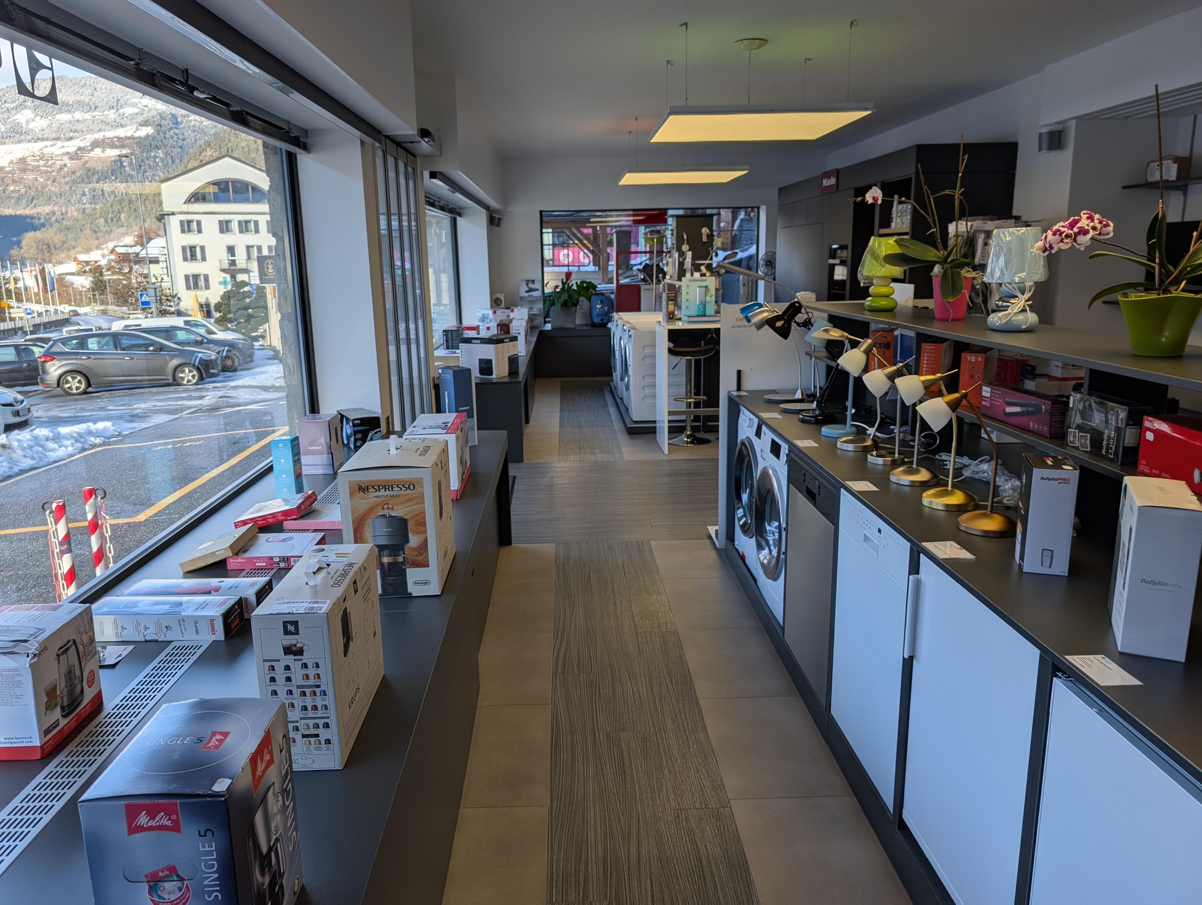 Intérieur chaleureux d'un showroom d'électroménager en Valais avec des appareils Miele et Nespresso exposés sous une lumière douce et des accents laiton
